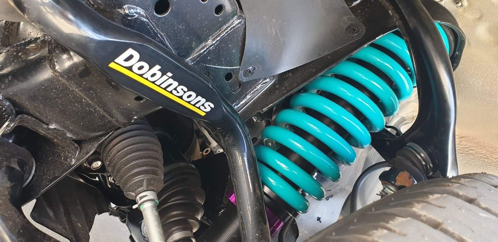 A teal coil spring and shock absorber fitted to a 4x4 suspension
