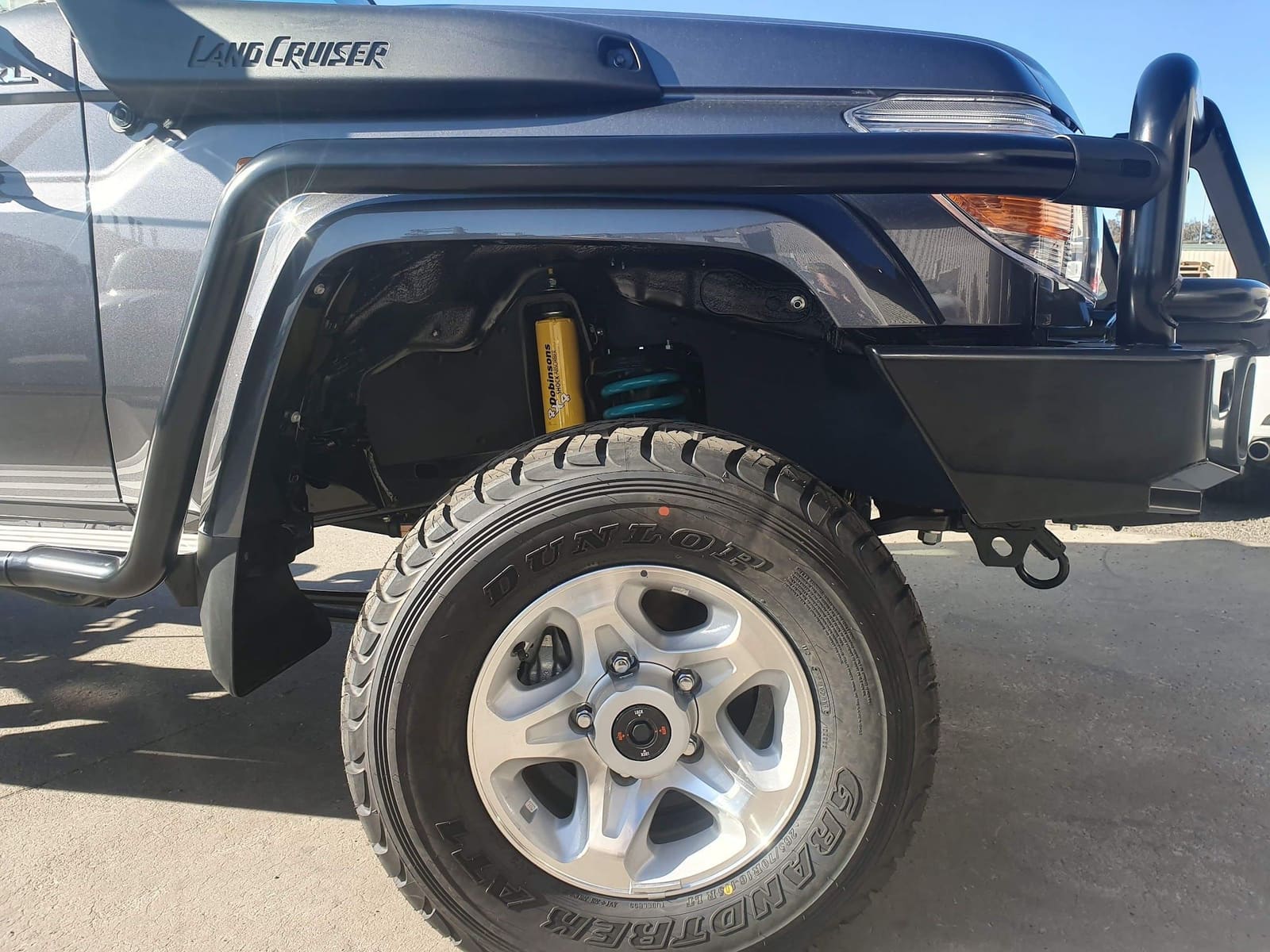 A dark grey Land Cruiser with a bull bar parked on the concrete outside the workshop