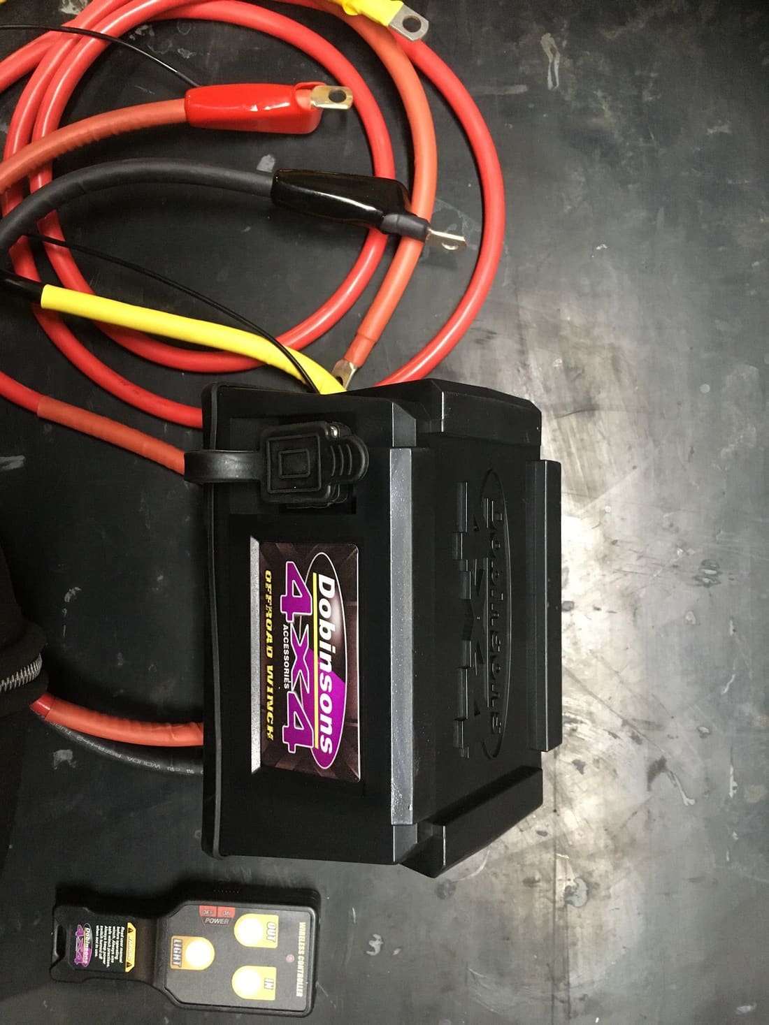 A battery with heavy red and black cables on a dark bench